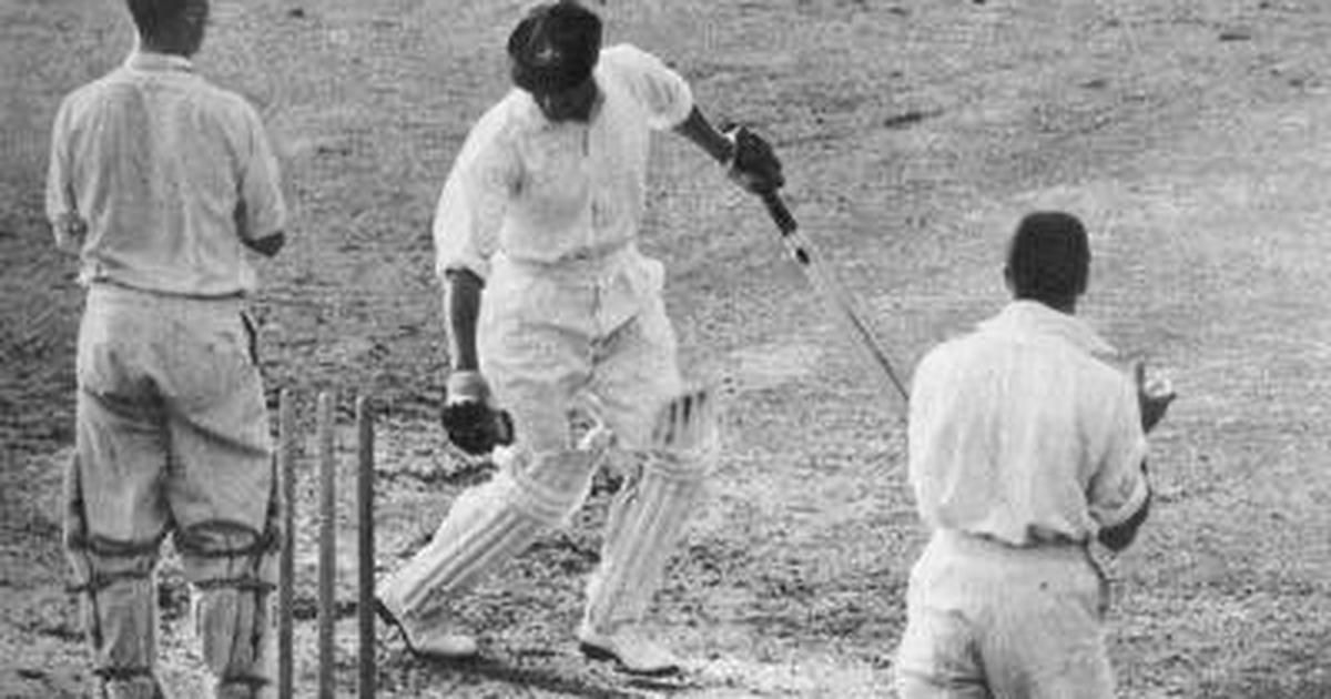 Sir Donald Bradman is standing with two other people, holding a bat.