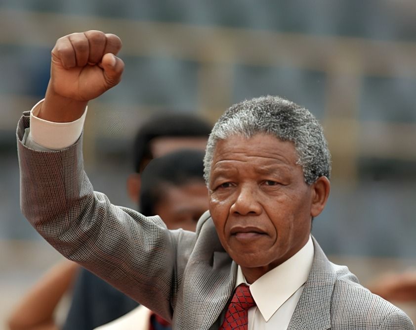 Nelson Mandela standing in a grey and white suit, raising his fist confidently.