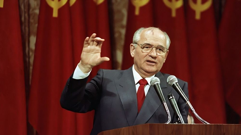 Leader giving speech with Soviet flags in the background, addressing an audience.