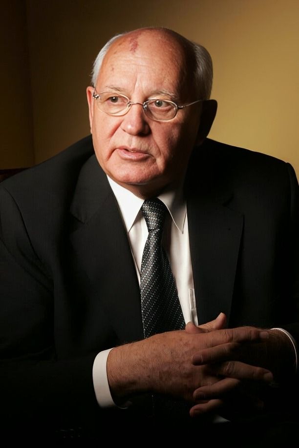 Distinguished elderly man in suit, seated with clasped hands, thoughtful expression.