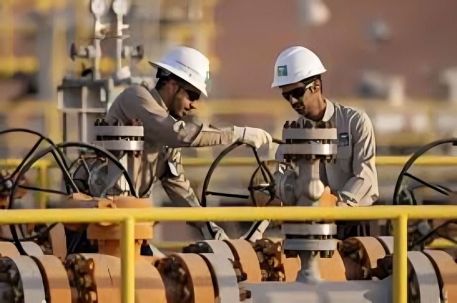 Two workers in hard hats operating valves at an oil refinery.