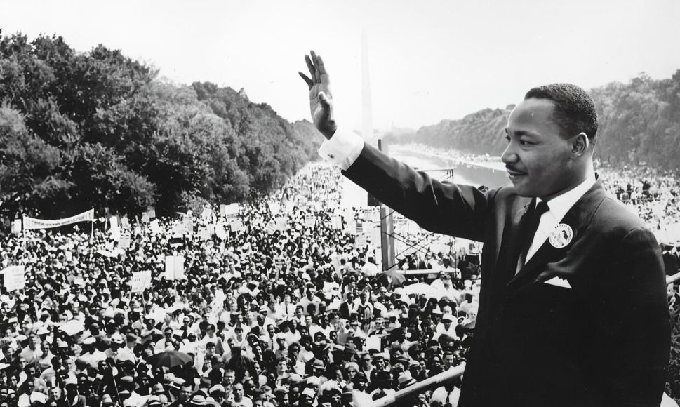 A black and white image of Martin Luther King Jr. addressing a large crowd.