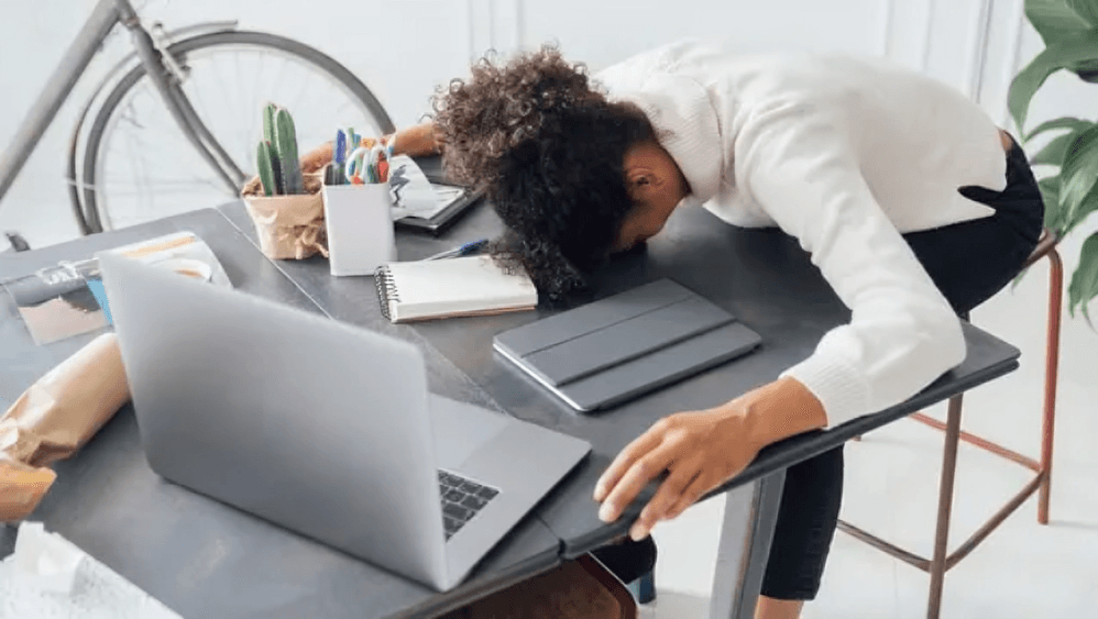 Exhausted woman with head on desk near laptop.
