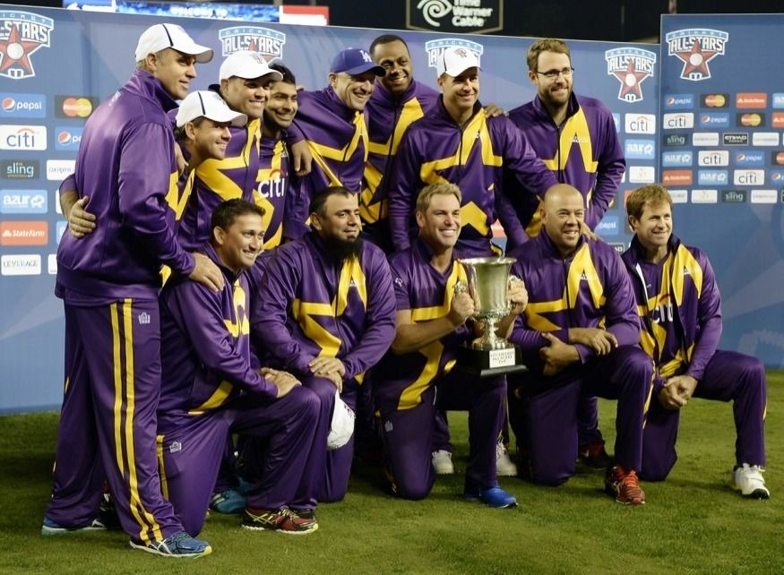 A cricket team dressed in purple celebrates while holding a trophy on the field with a backdrop.