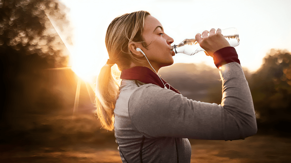 A woman drinking water, illuminated by golden hour sunlight.