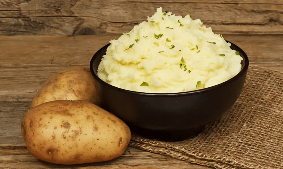 A bowl of mashed potatoes and two whole potatoes.