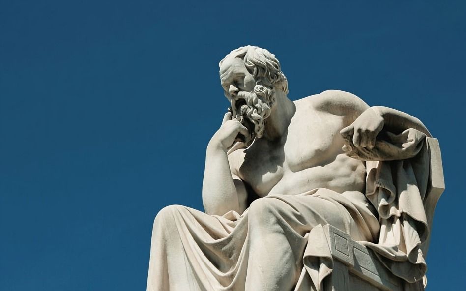 A marble statue of an ancient philosopher, deep in thought, against a clear blue sky background.