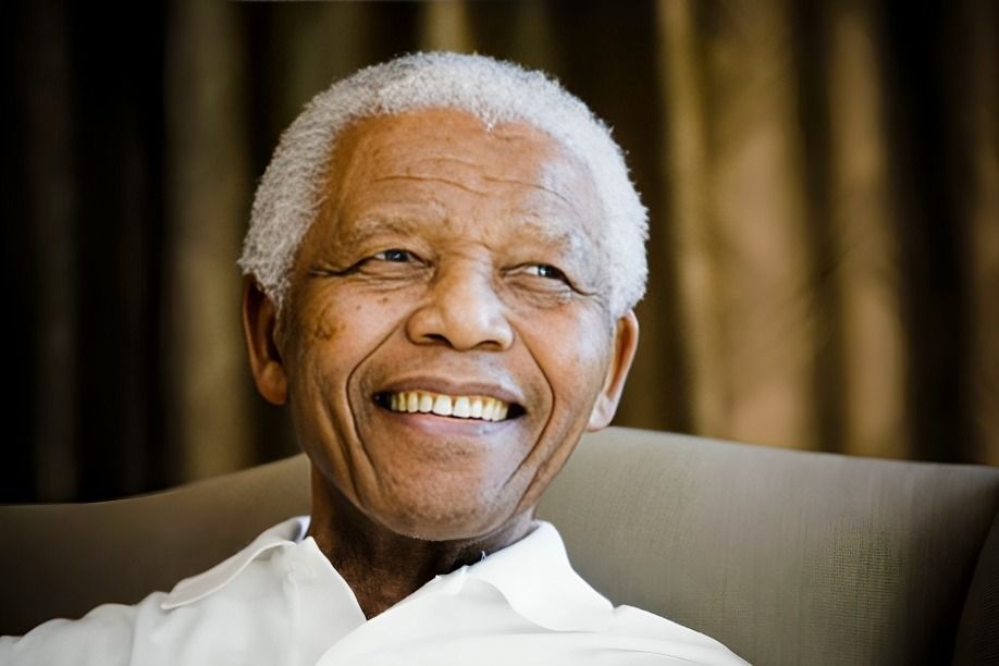 Nelson Mandela smiling warmly while seated against a dark background, exuding peace and positivity.