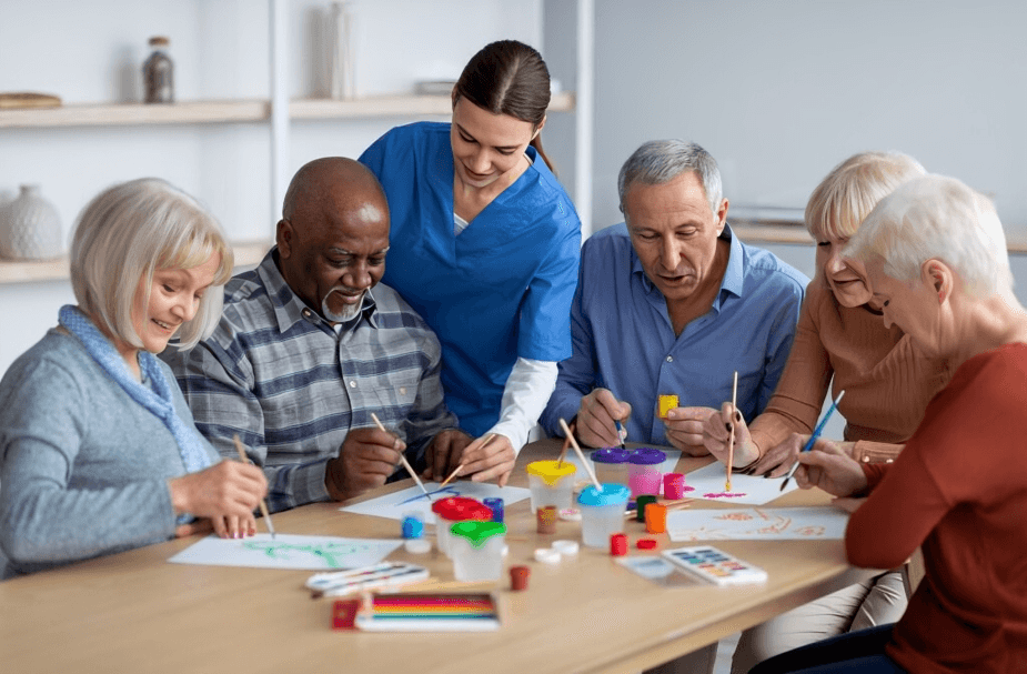 Seniors and caretaker happily painting together at a table.
