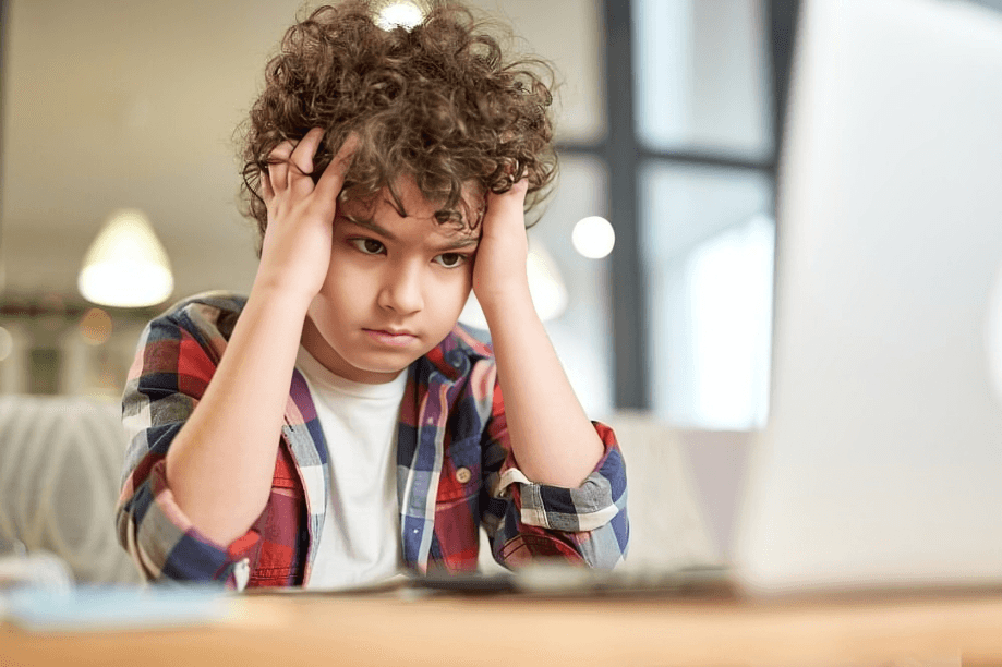 A curly-haired boy looking frustrated at a laptop.