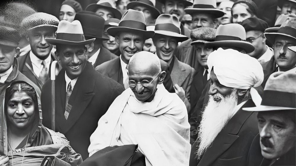 Mahatma Gandhi standing amidst a crowd of people.