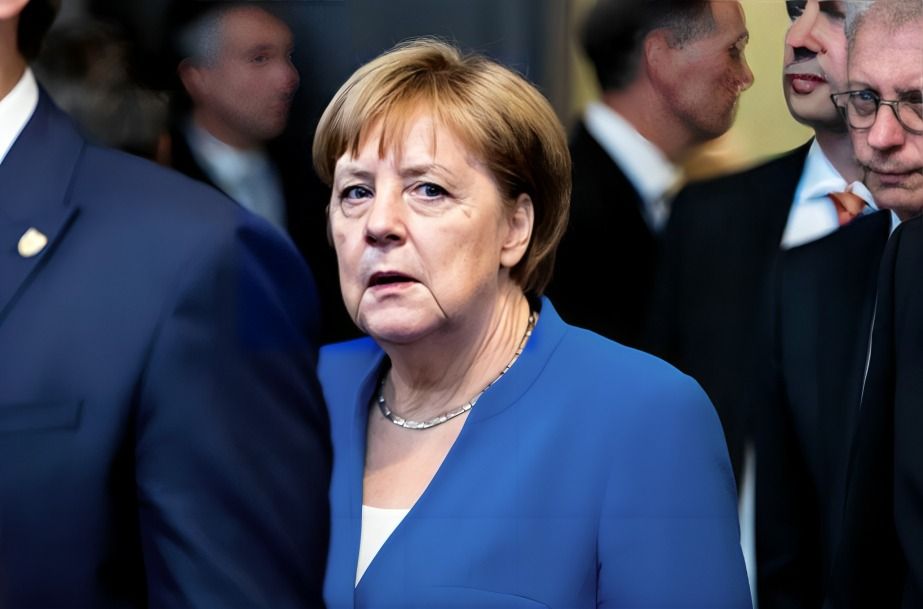 Angela Merkel in a blue blazer, appearing thoughtful in a crowded setting.