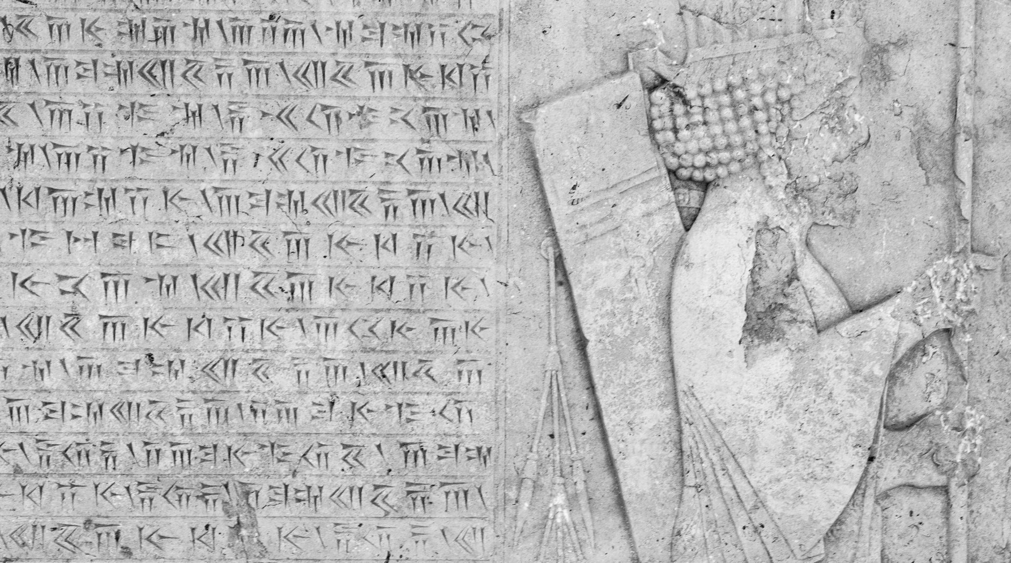 Grayscale image of a weathered stone slab with cuneiform inscriptions. 