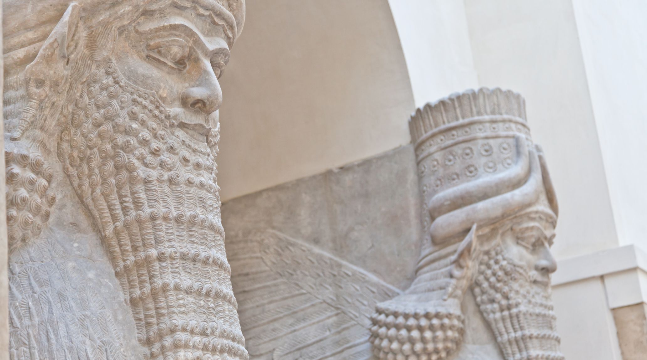 Ancient Assyrian winged statues with detailed beards and crowns carved in stone.