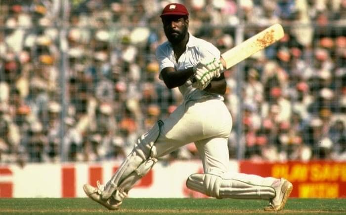 A cricket player in a white uniform is in mid-air, swinging a bat.