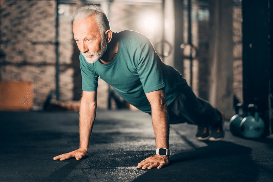 A senior man doing push-ups in a gym.