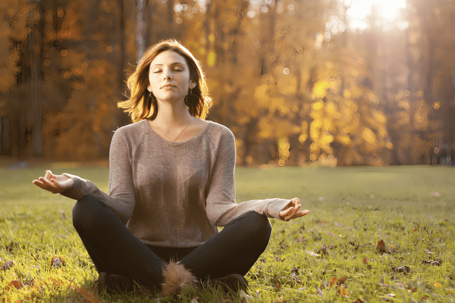 A woman meditating in a green forest.