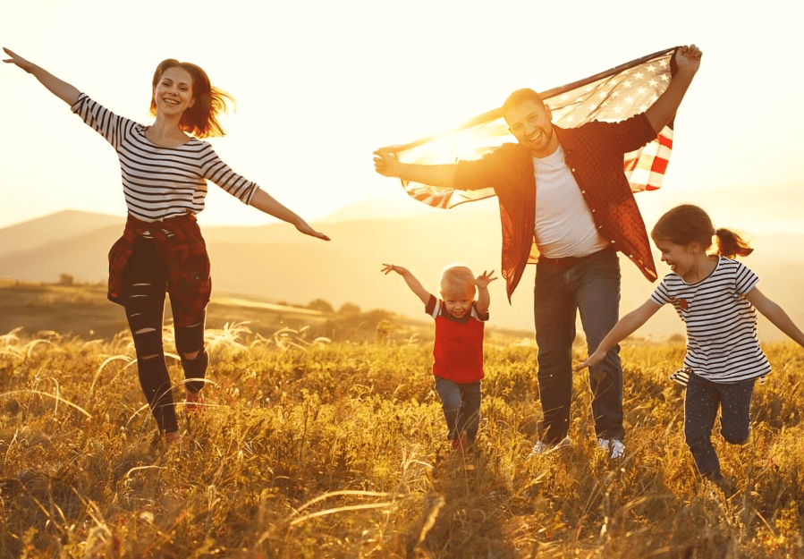 Family running in a field with American flag at sunset.