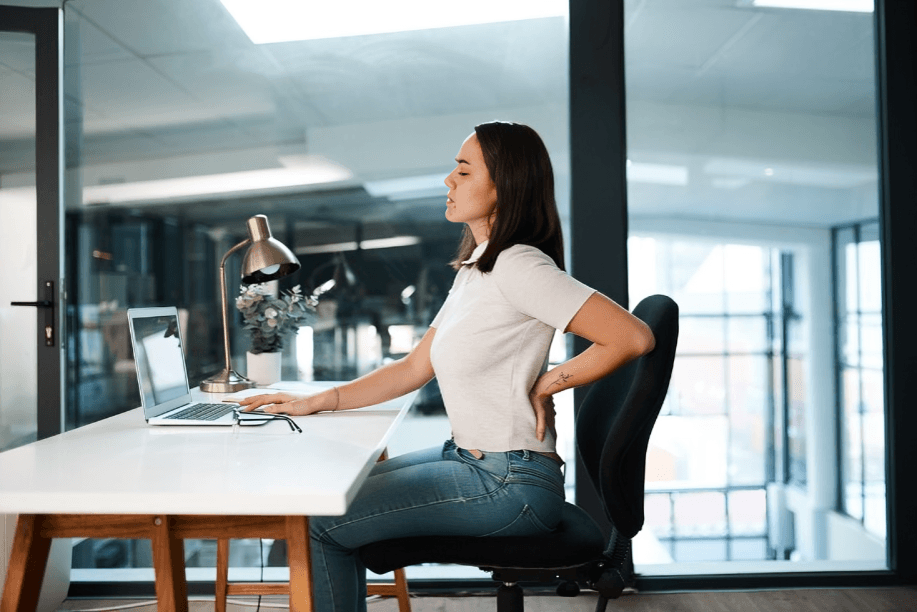 Woman at desk with laptop, experiencing back pain.
