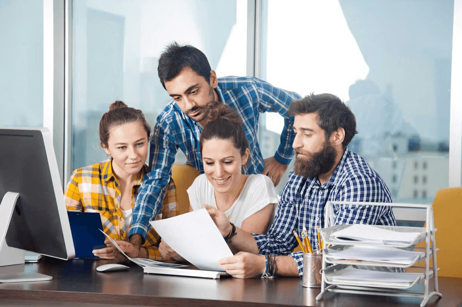 Four people collaborating around a desk with documents.