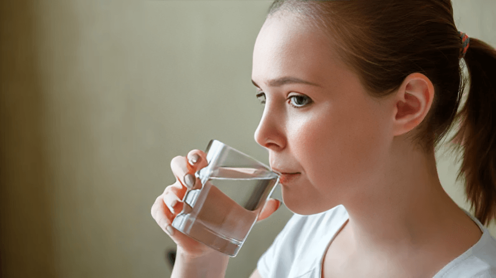 A young woman drinking clear water from a glass.