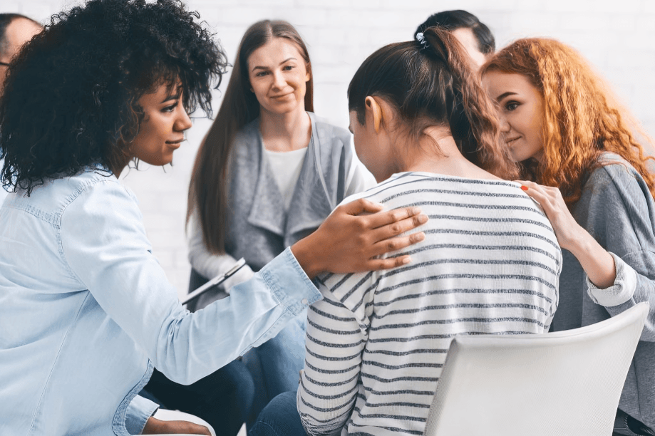 A diverse support group comforts a distressed woman.