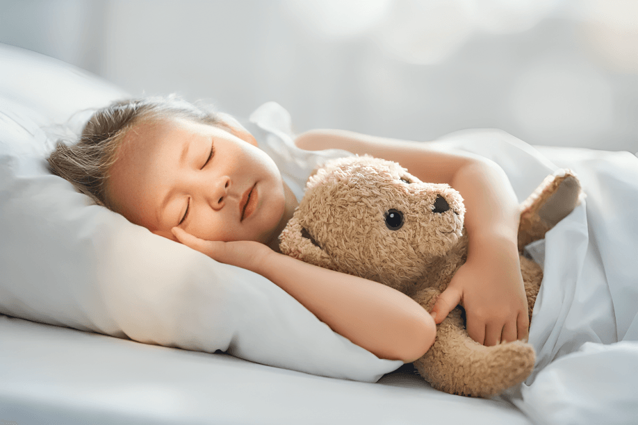Young child sleeping peacefully with teddy bear in bed.