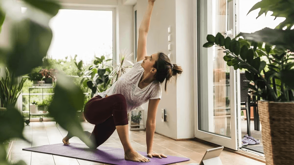 A woman doing yoga indoors with an arm raised.