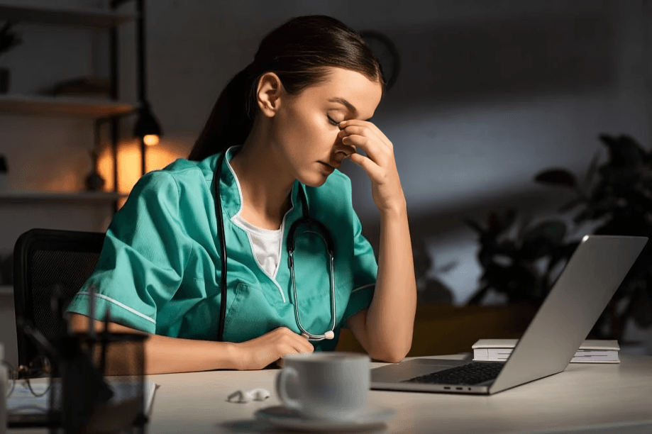A seemingly tired female doctor with a laptop and coffee.