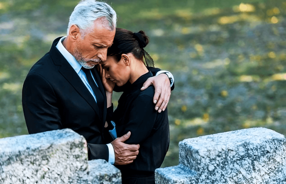 A man comforts a grieving woman at a graveside.