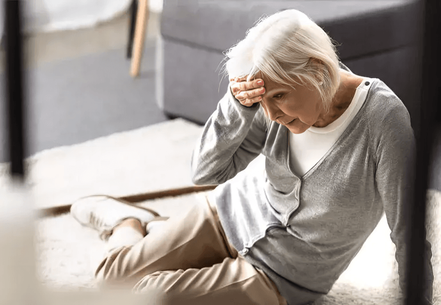 An elderly woman fallen on the floor, holding her head.