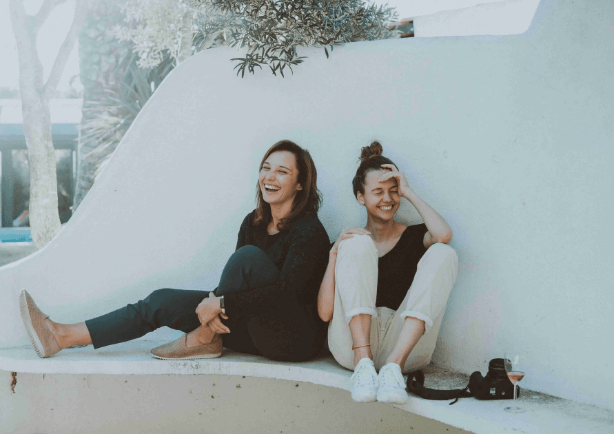 Two young women laughing while sitting outdoors.