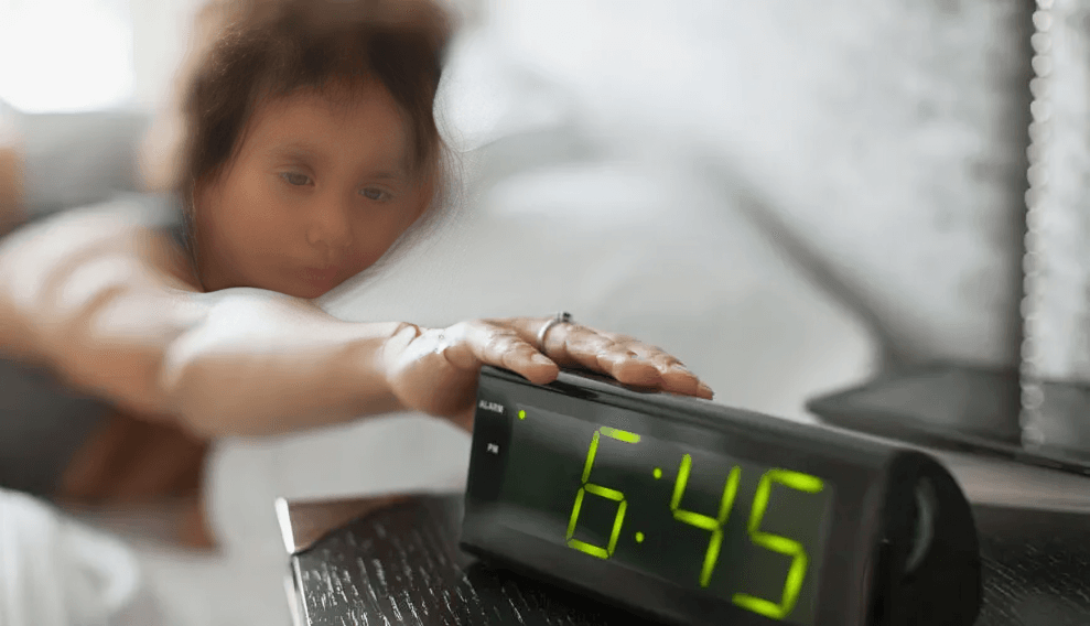 Person reaching for a digital alarm clock displaying 6:45.