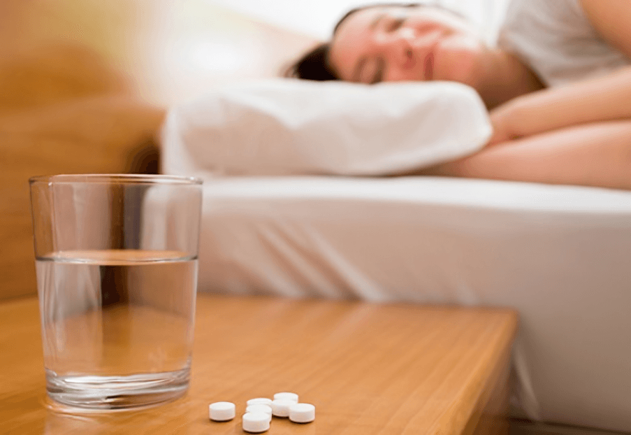 Water glass and pills on nightstand, sleeping woman.