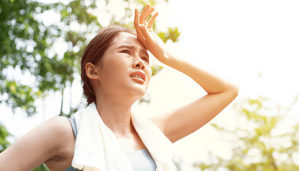 A woman standing with her hand on her head on a sunny day.