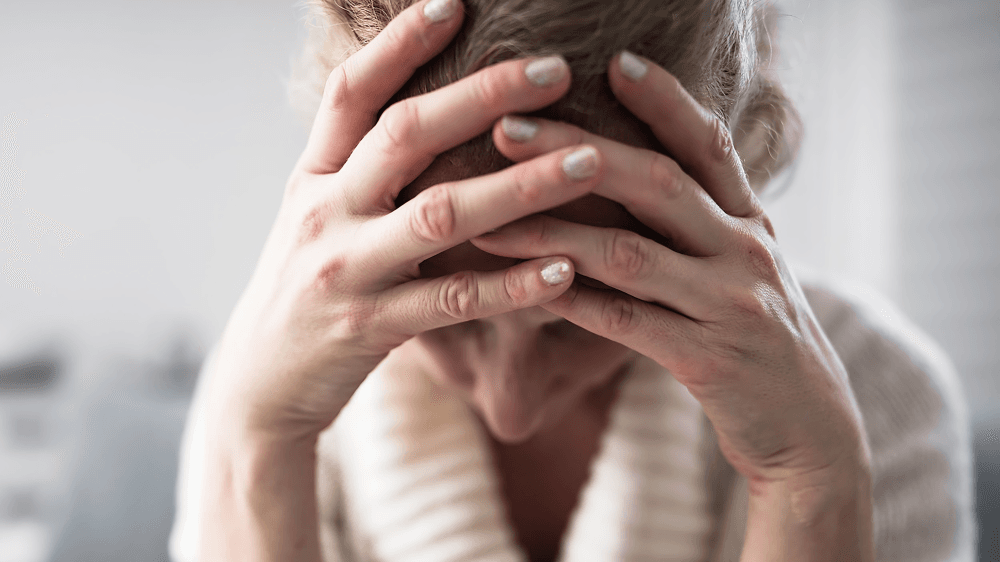 A close-up of a woman holding her head in distress.
