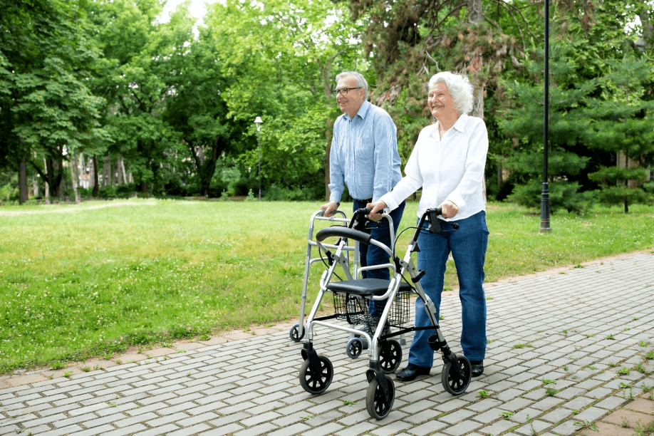 An elderly couple strolling in the park with mobility aids.