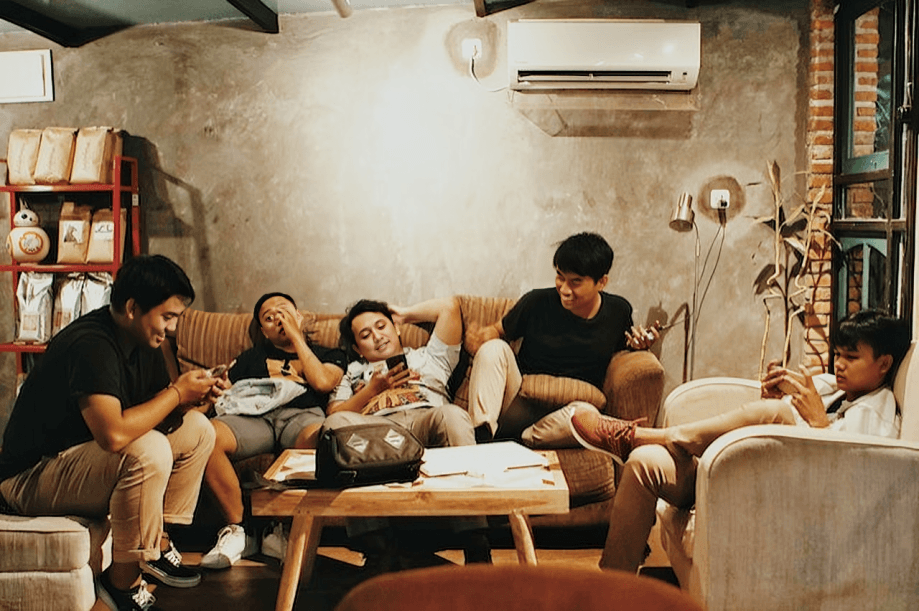 Five young men relaxing and using their phones indoors.