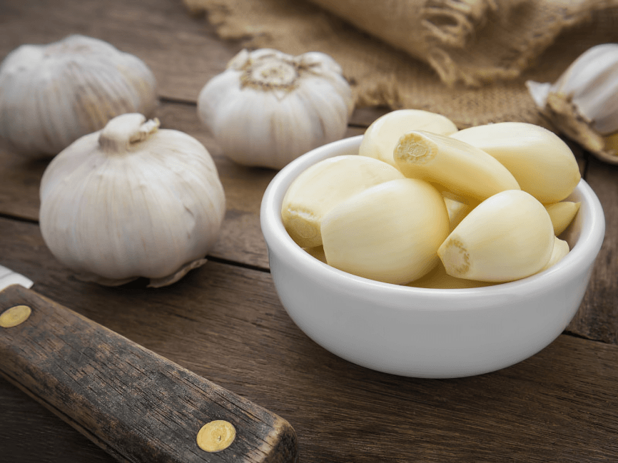 A bowl of peeled garlic cloves with whole bulbs.