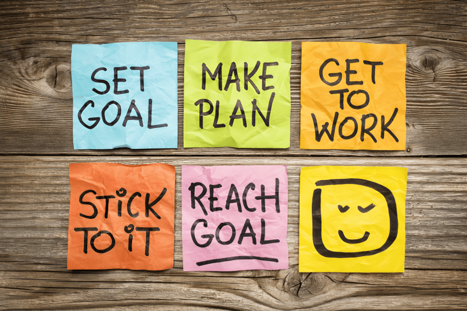 Six colorful sticky notes on wood: goal-setting steps.