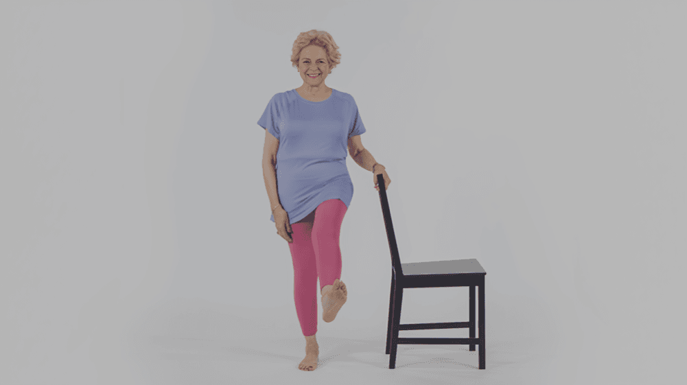 Smiling woman balancing on one leg with a chair.