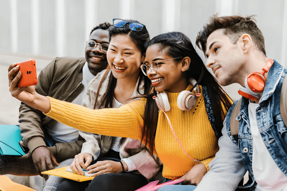 A diverse group of young adults taking a selfie outdoors.