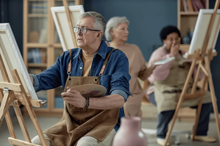 An elderly man painting in an art class.