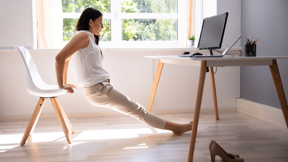 Woman performing chair dips in a bright office.