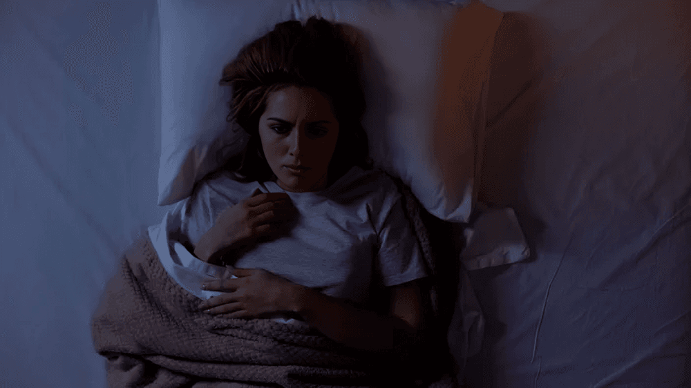 Worried woman lying awake in a dark bed.
