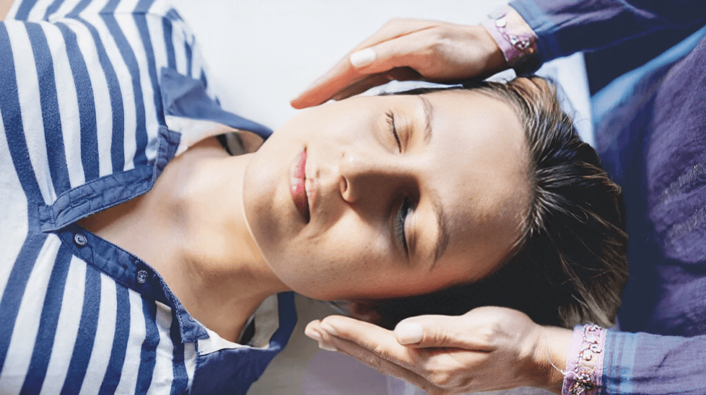 Hands performing reiki on a woman's head.