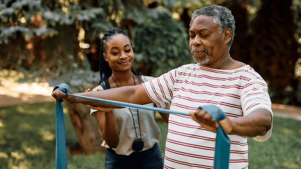 A senior man exercising with a resistance band, assisted.