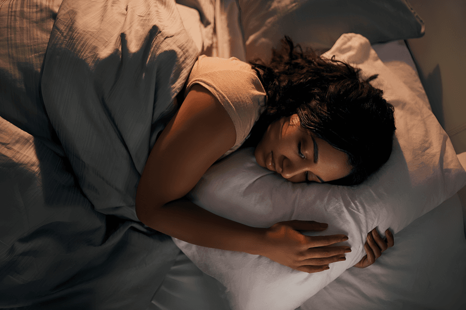 A person with dark hair sleeps peacefully in bed.