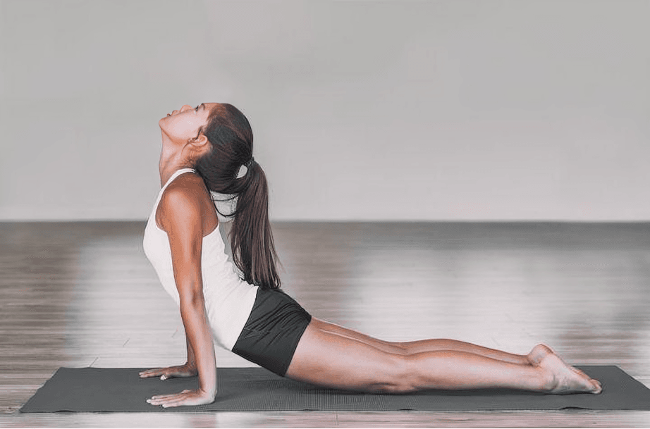 Woman in white top performing upward-facing dog yoga pose.