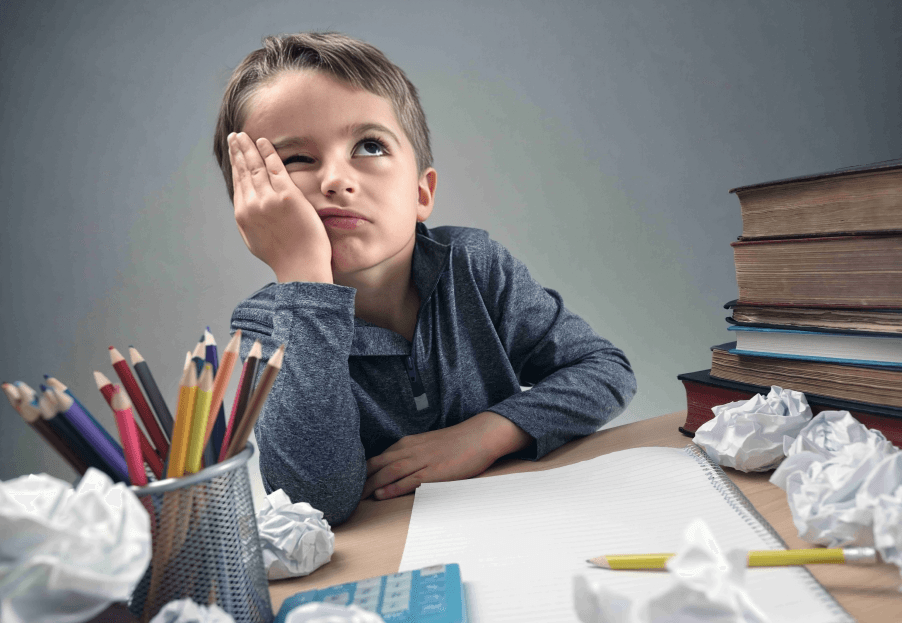 Boy with frustrated expression at desk with school supplies.